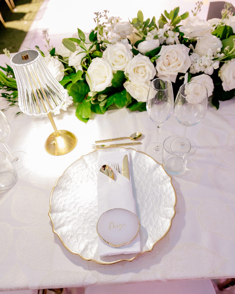 Place setting with a scalloped gold-rimmed plate, name card and white florals, Chic Bahamas Weddings