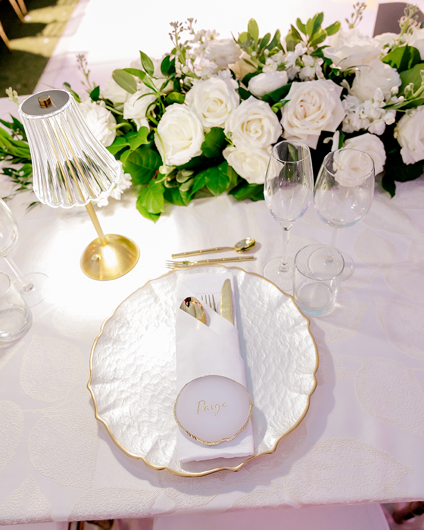 Place setting with a scalloped gold-rimmed plate, name card and white florals, Chic Bahamas Weddings