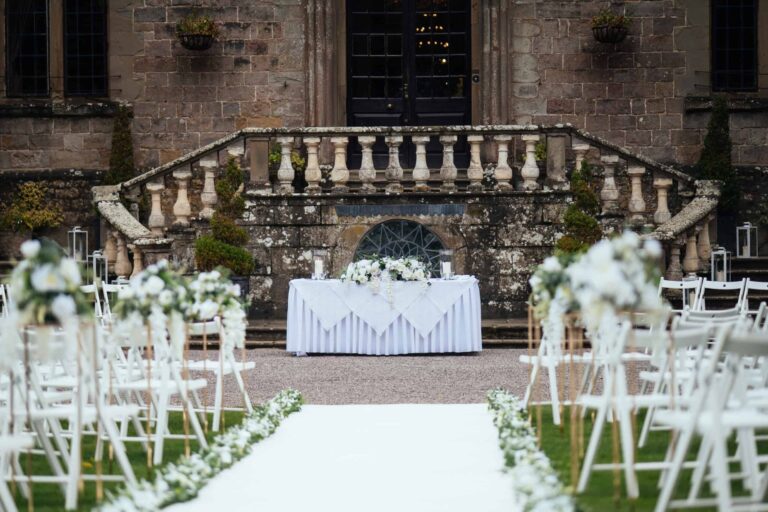 An outdoor ceremony on the terrace, the balustraded steps and registrar's table dressed with white florals, Clearwell Castle