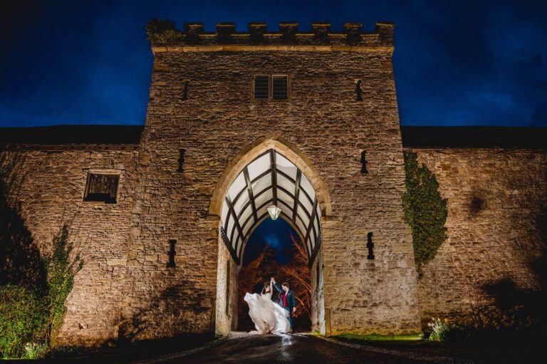 A couple beneath the floodlit gatehouse tower and pointed arch after dark, Clearwell Castle