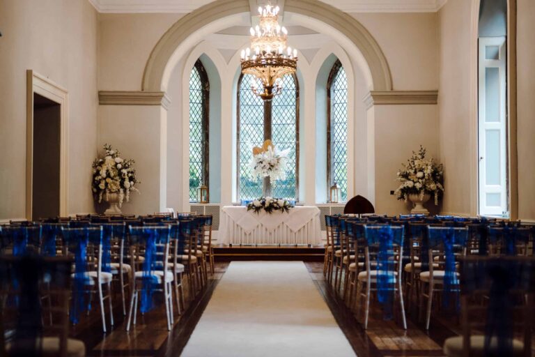 A Ballroom ceremony with blue sashes, the registrar's table below the arched leaded window and chandelier, Clearwell Castle