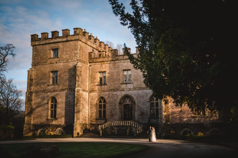 The castle's tower and terrace steps in golden evening light, the couple small beneath it, Clearwell Castle