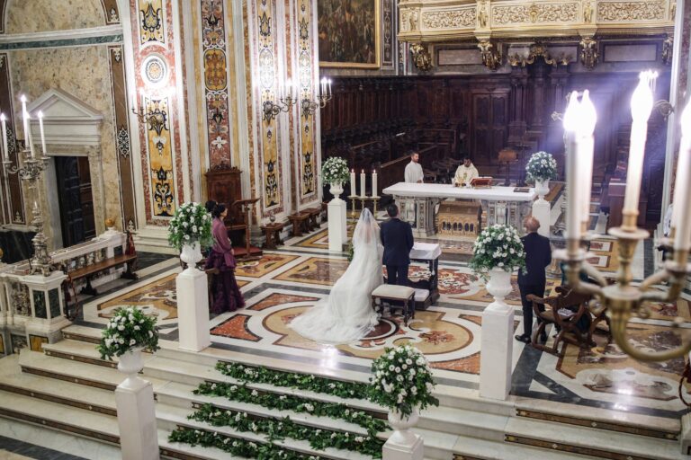A church ceremony seen from above: urns of white flowers on pedestals and garlands of leaves laid along the altar steps, Clorinda Bellone Elite Weddings