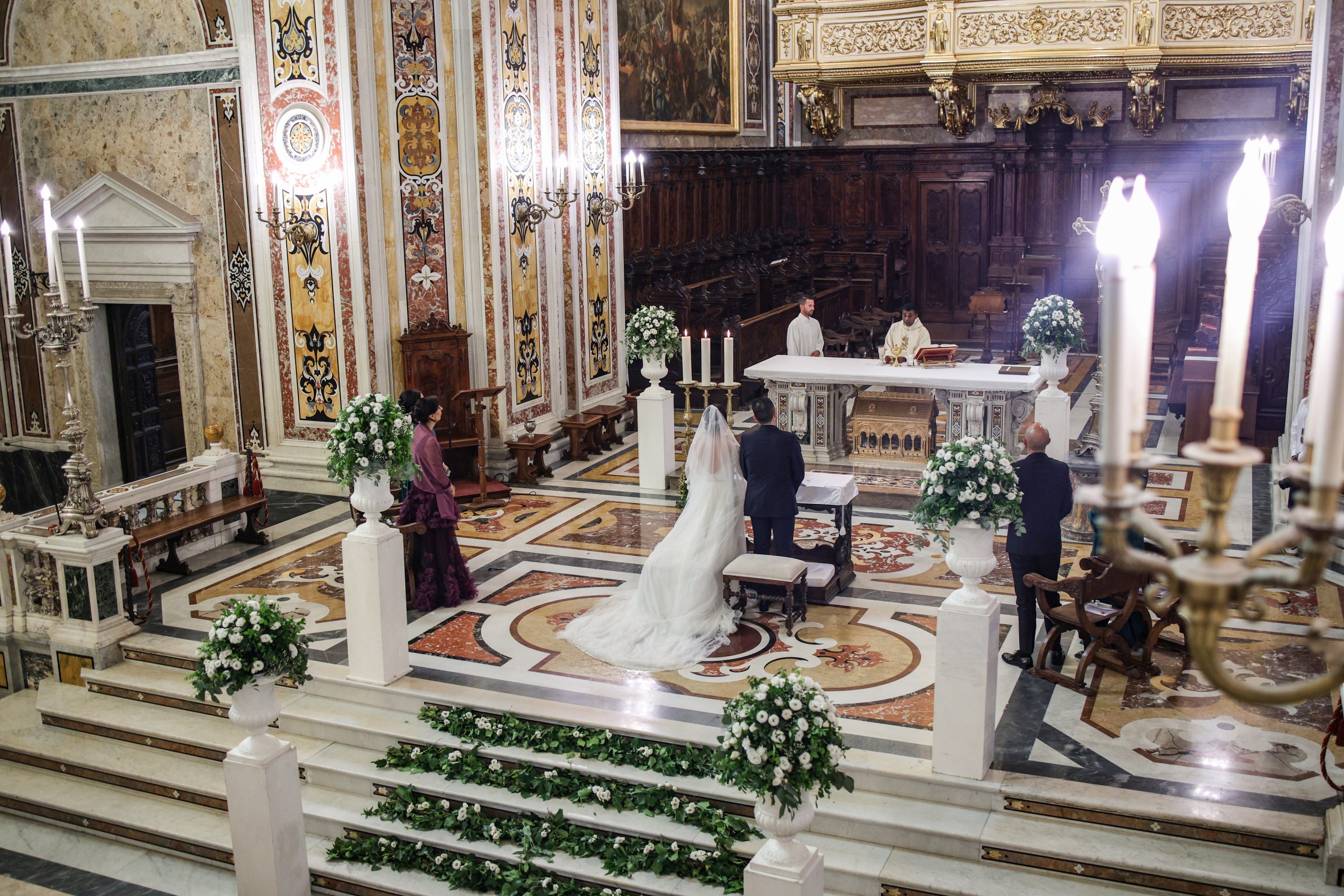 A church ceremony seen from above: urns of white flowers on pedestals and garlands of leaves laid along the altar steps, Clorinda Bellone Elite Weddings