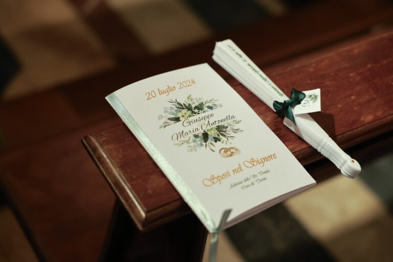 Order of service for a July 2024 wedding at the Abbazia della Santissima Trinità in Cava de' Tirreni, with a fan tied in green ribbon, Clorinda Bellone Elite Weddings