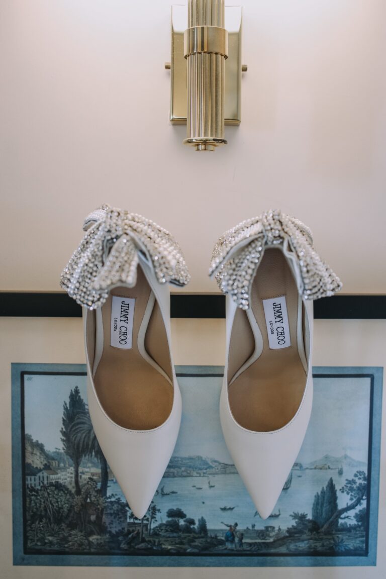 Bridal shoes hung on a white wall above a framed antique coastal print, Clorinda Bellone Elite Weddings