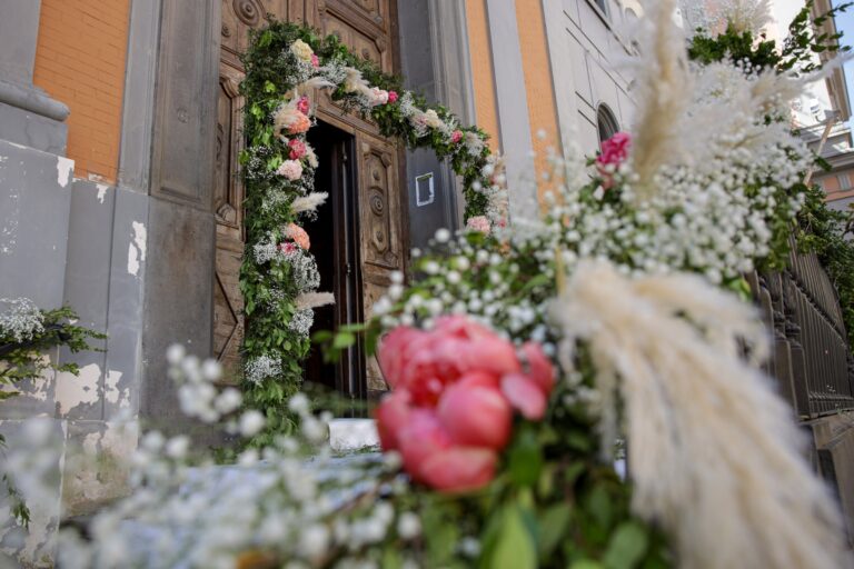 A church doorway framed with greenery, white flowers, coral peonies and pampas grass, Clorinda Bellone Elite Weddings