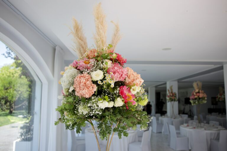 A tall centrepiece of hydrangeas, roses and pampas grass in a white reception room overlooking a garden, Clorinda Bellone Elite Weddings