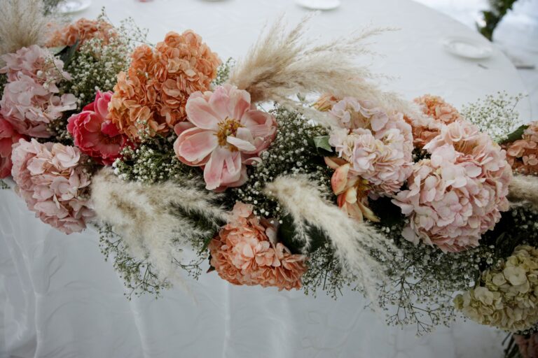 A table garland of peach hydrangeas, coral peonies, gypsophila and pampas on white linen, Clorinda Bellone Elite Weddings