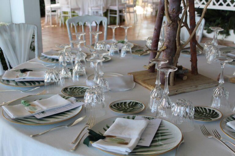 A round table laid with crystal, monstera-leaf plates and a centrepiece of bare branches, Clorinda Bellone Elite Weddings