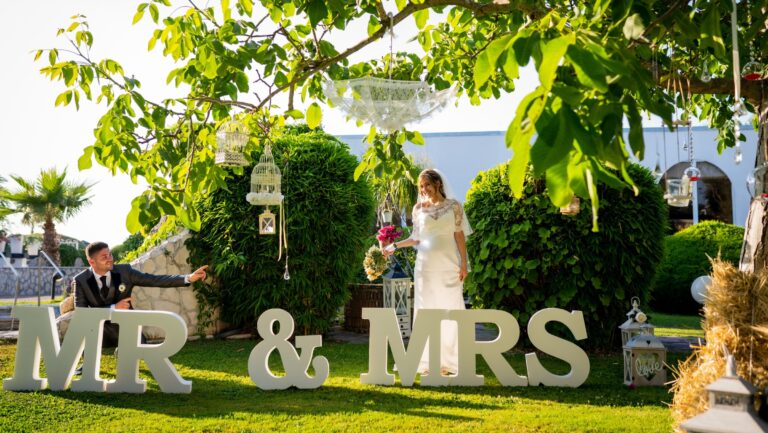 A couple in a garden with large MR & MRS letters on the lawn and lanterns and birdcages hanging from the trees, Clorinda Bellone Elite Weddings