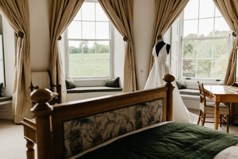 A bedroom with window seats over the park and a wedding dress on a stand, ready for getting ready, Cluny Castle