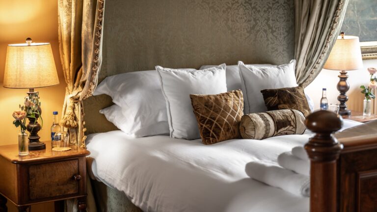 A canopied bed with white linen and lit lamps on the bedside tables, Cluny Castle