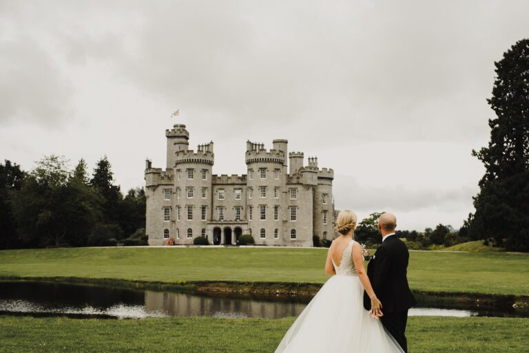 A bride and groom seen from behind, looking across the pond to the castle, Cluny Castle