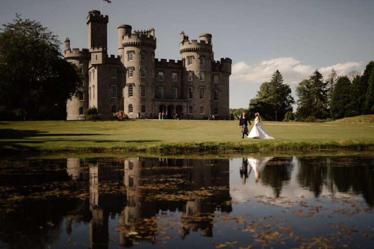 A couple walking on the lawn by the pond, with the castle and its reflection behind, Cluny Castle