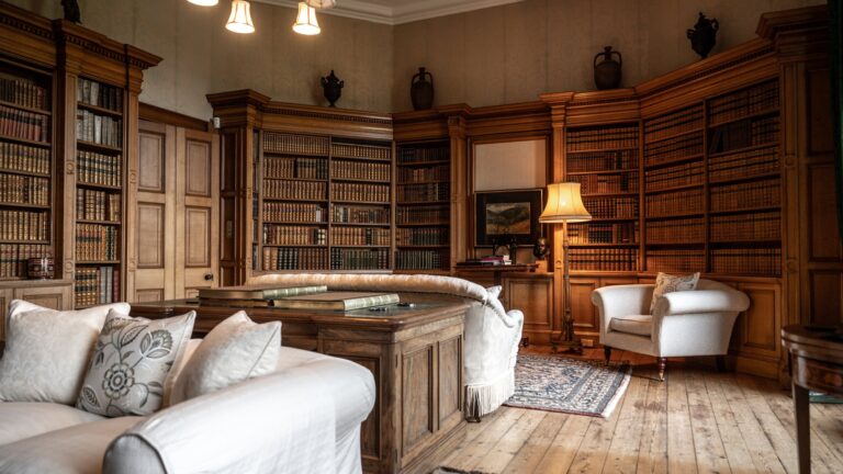The panelled Library lined with bookcases, with sofas and an armchair on bare boards, Cluny Castle