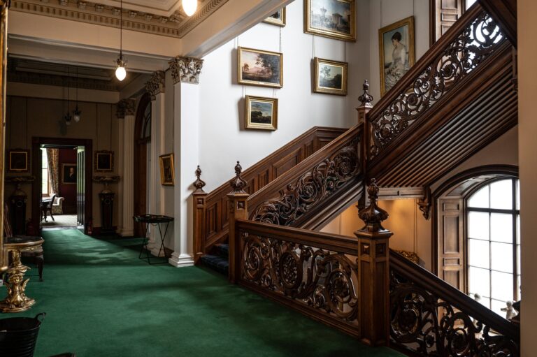 The main staircase with its carved timber balustrade, green carpet and paintings on the walls, Cluny Castle