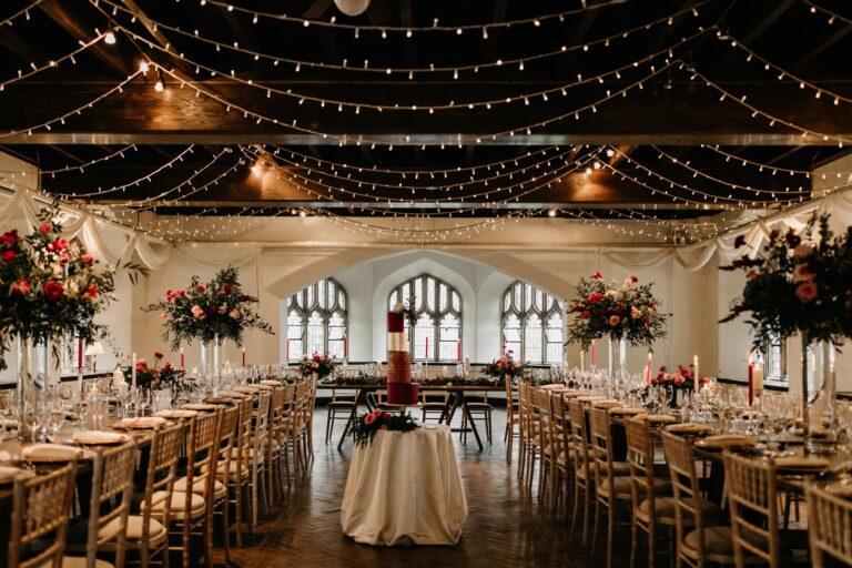 The Tenants' Hall laid with long tables for a wedding dinner under a canopy of fairy lights, the cake at the centre, Cluny Castle