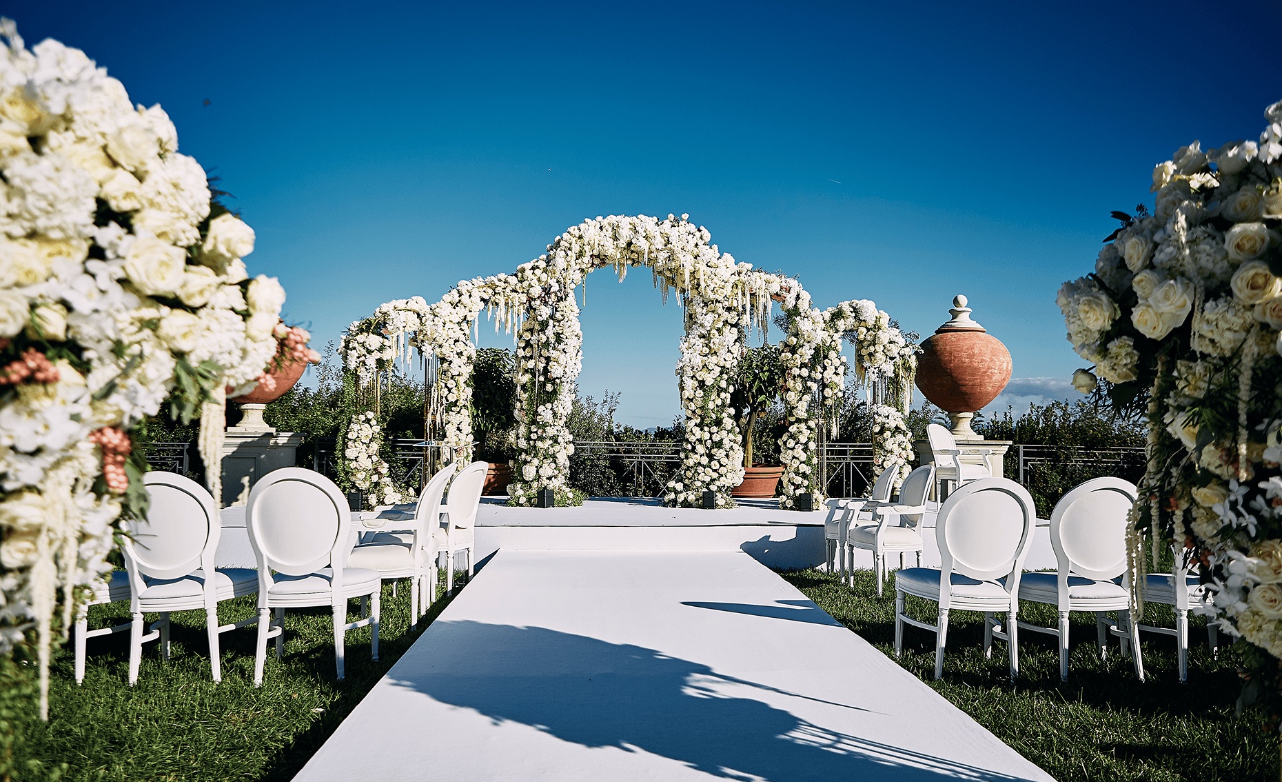 White aisle lined with chairs and floral arches in a garden, Cocoon Events