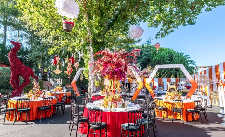 Round tables dressed in red and orange under trees, Cocoon Events