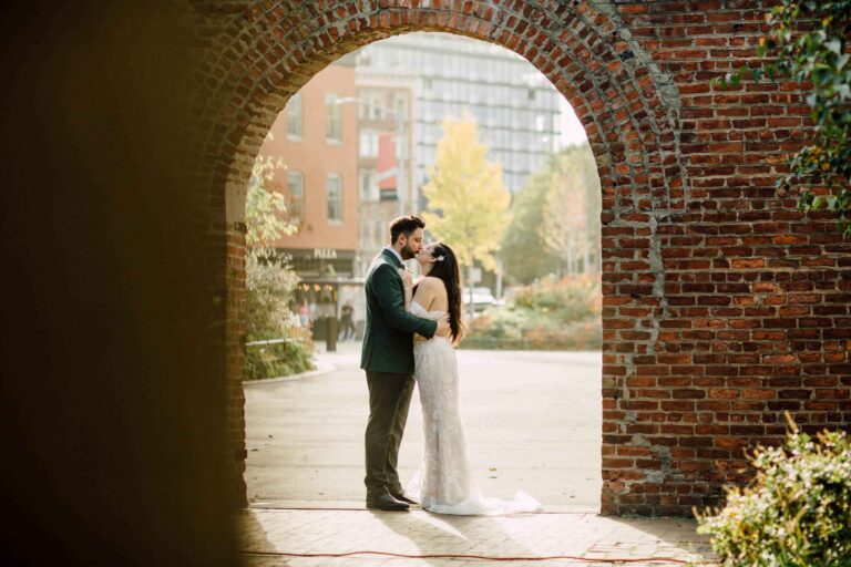 The couple framed by a brick archway in autumn, from a wedding in DUMBO, Brooklyn, Cottonwood Studios