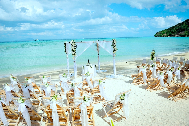 A ceremony set-up of cream chairs on a white beach beside turquoise water in Thailand, Creative Events Asia