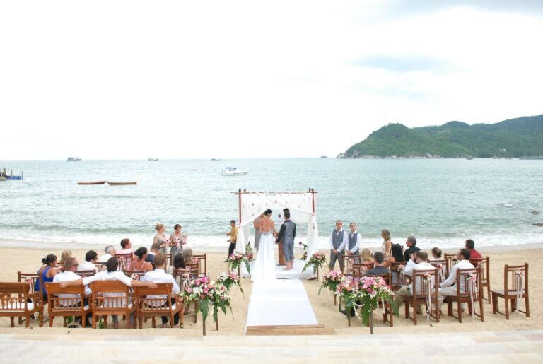 A ceremony under a white canopy on a beach below forested hills, Creative Events Asia
