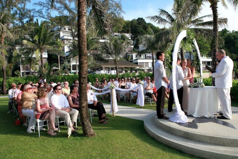 A couple at a ceremony on a raised platform on a resort lawn, with guests seated beneath palms, Creative Events Asia