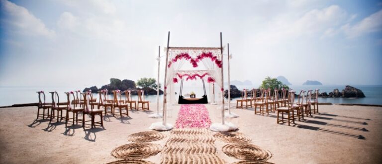 A pink-draped arch and aisle on a rocky shore with chairs set either side, Creative Events Asia