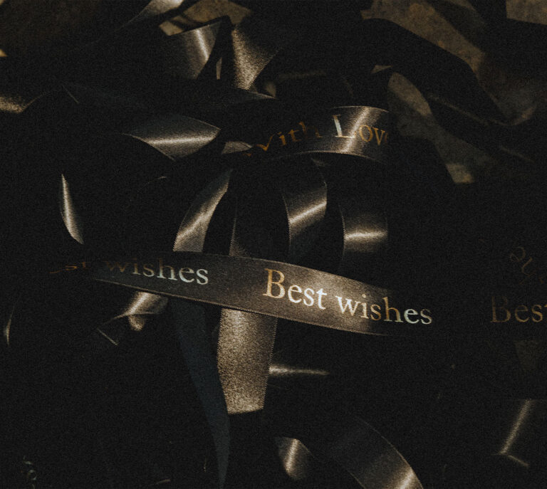 Black ribbon printed in gold with a personal message, Creed