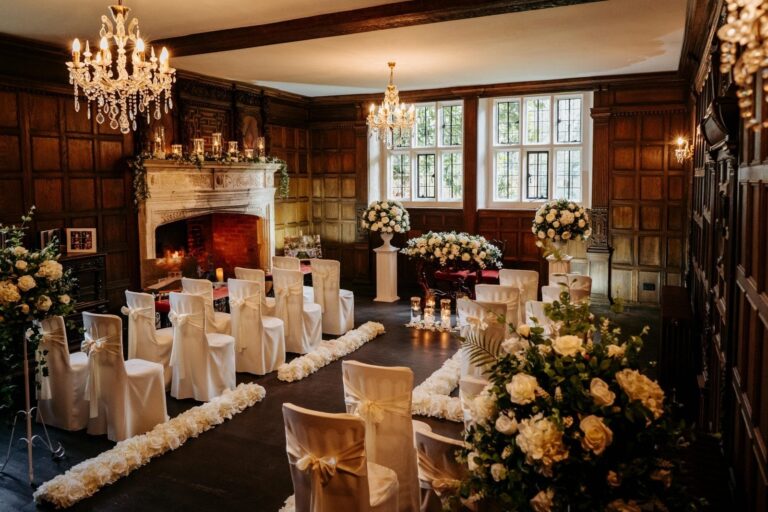 The Panelled Room laid for a civil ceremony, oak panelling, two chandeliers and a lit stone fireplace, Creeksea Place