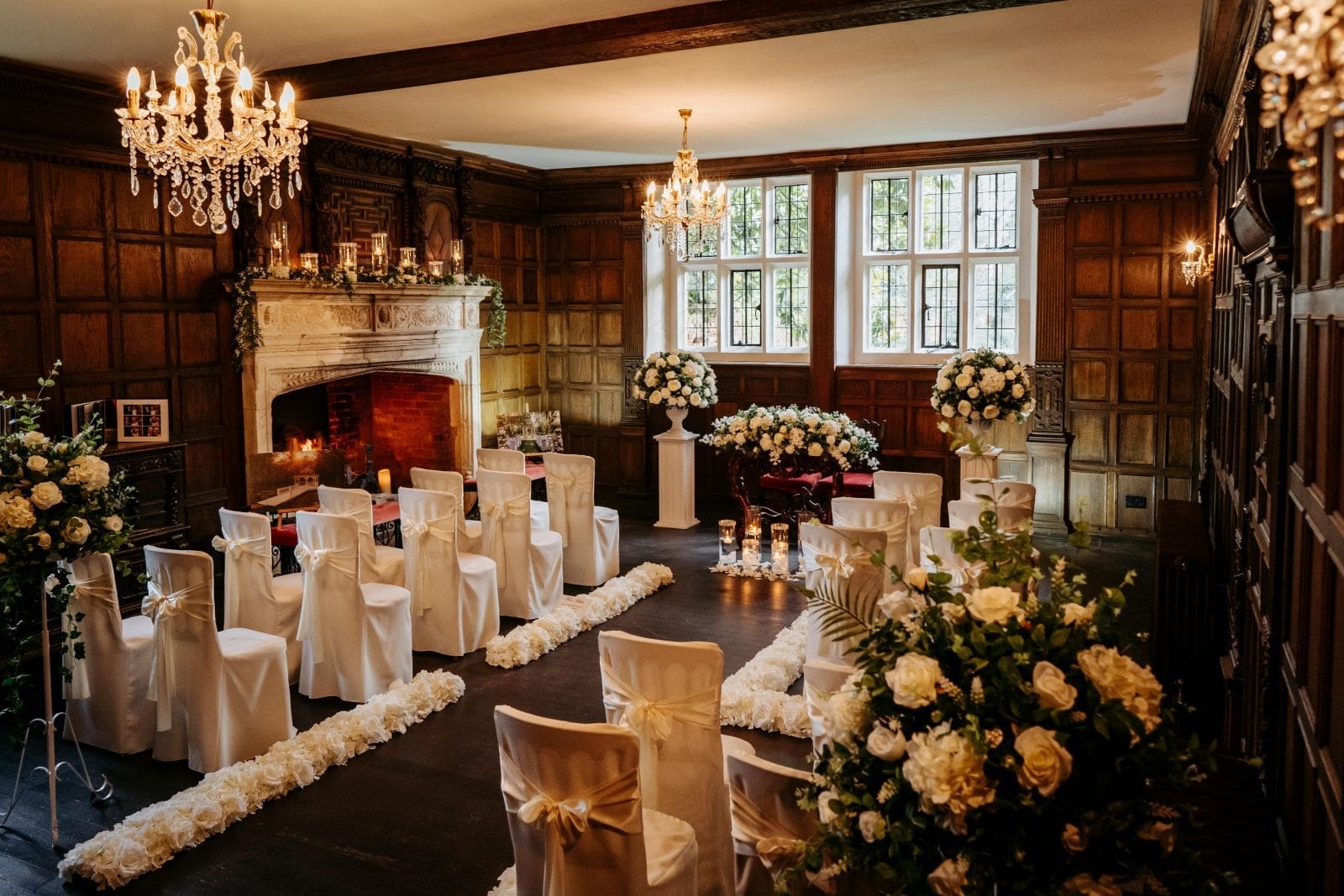 The Panelled Room laid for a civil ceremony, oak panelling, two chandeliers and a lit stone fireplace, Creeksea Place