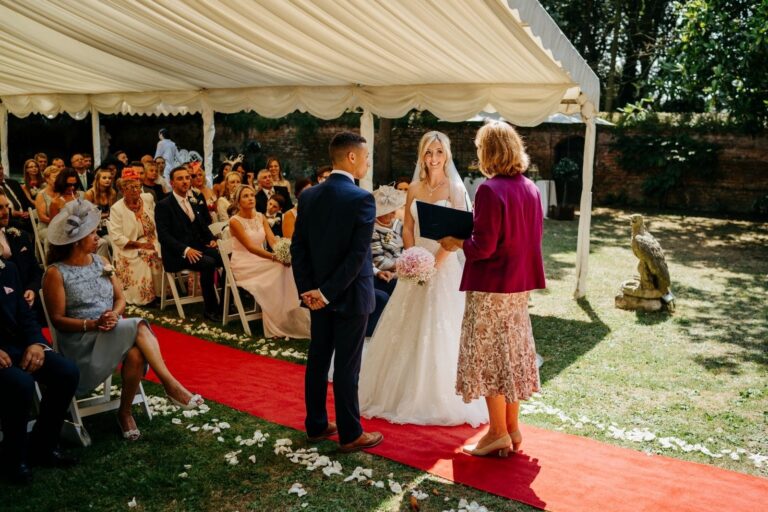 A ceremony under the silk canopy on the lawn, guests seated and the registrar officiating, Creeksea Place