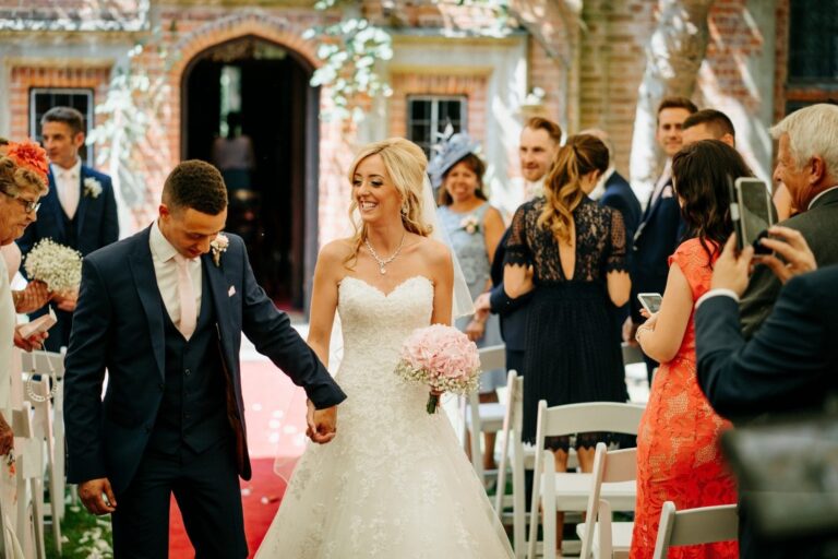 The aisle exit through the Tudor doorway, guests applauding, Creeksea Place