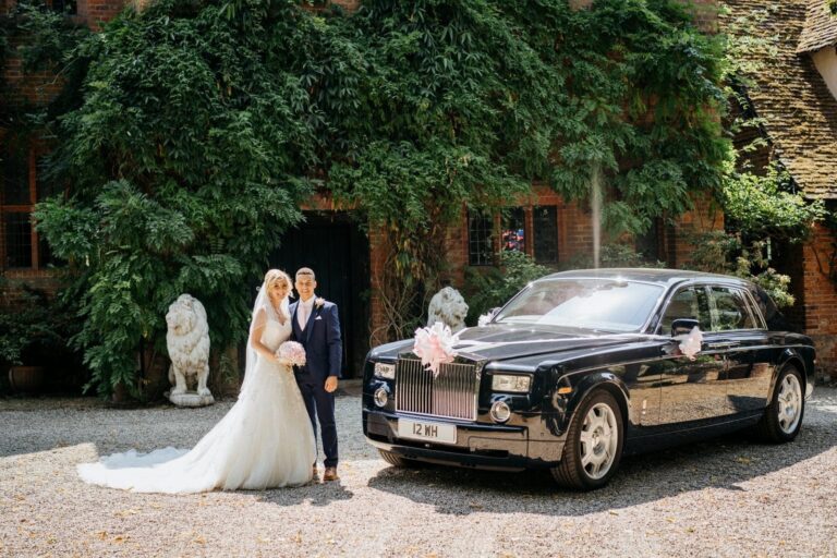 The couple beside a Rolls-Royce Phantom on the gravel court, wisteria-clad Tudor brick and stone lions behind, Creeksea Place