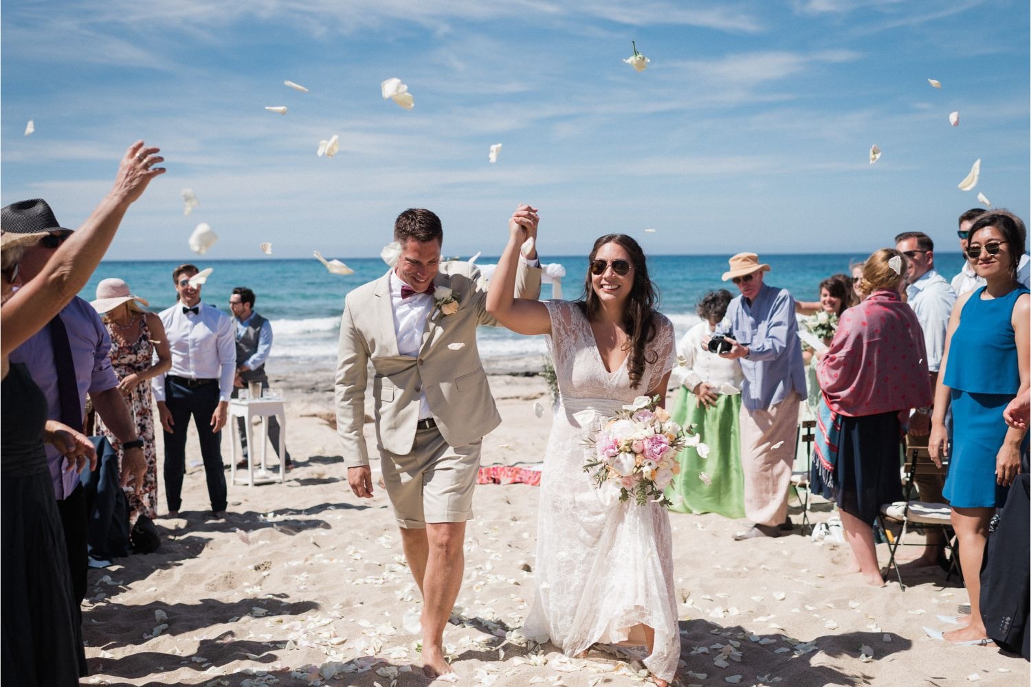 A newly married couple walk up a Cretan beach as guests throw petals, Crete for Love