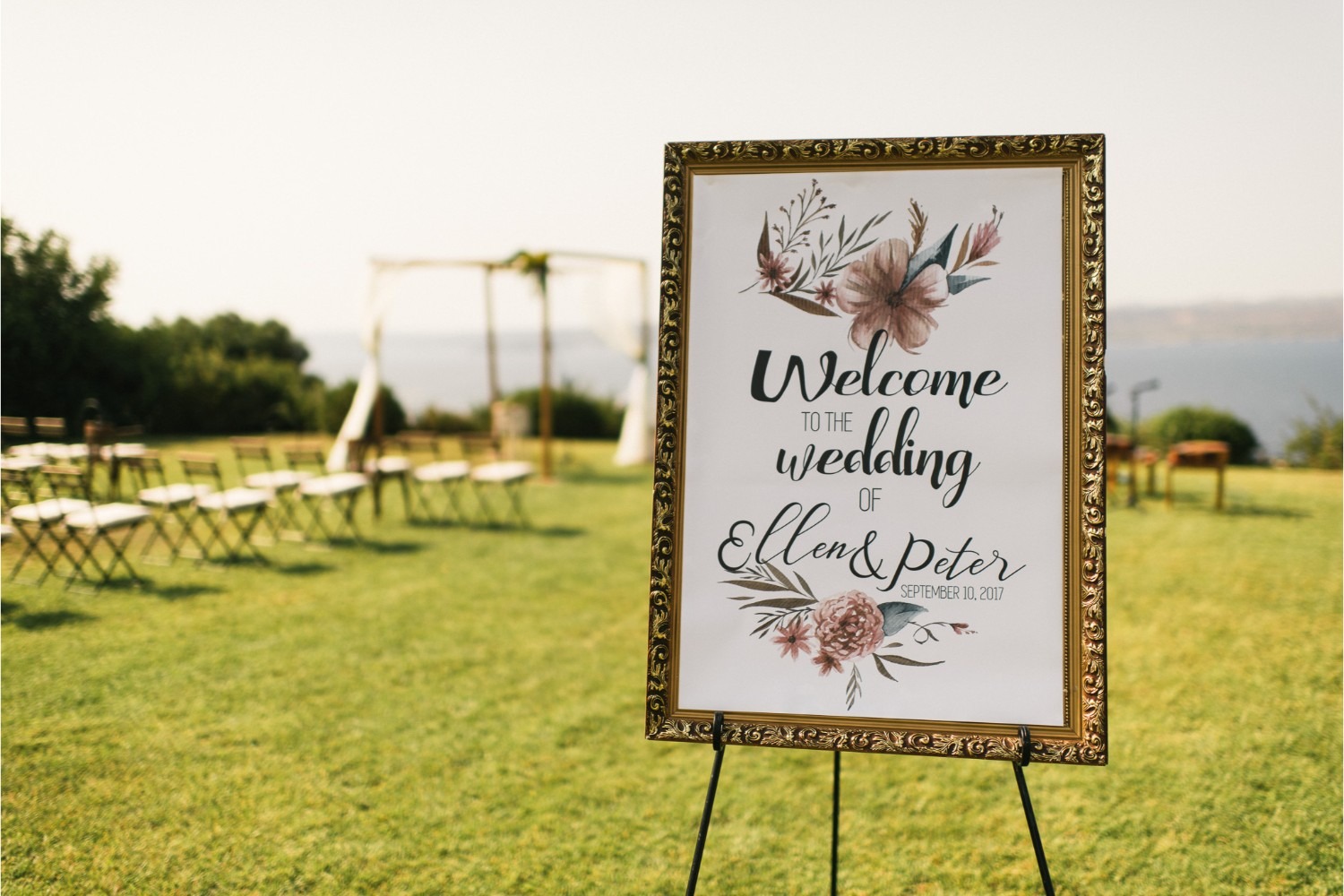 A framed welcome sign beside rows of chairs for a lawn ceremony above the sea, Crete for Love