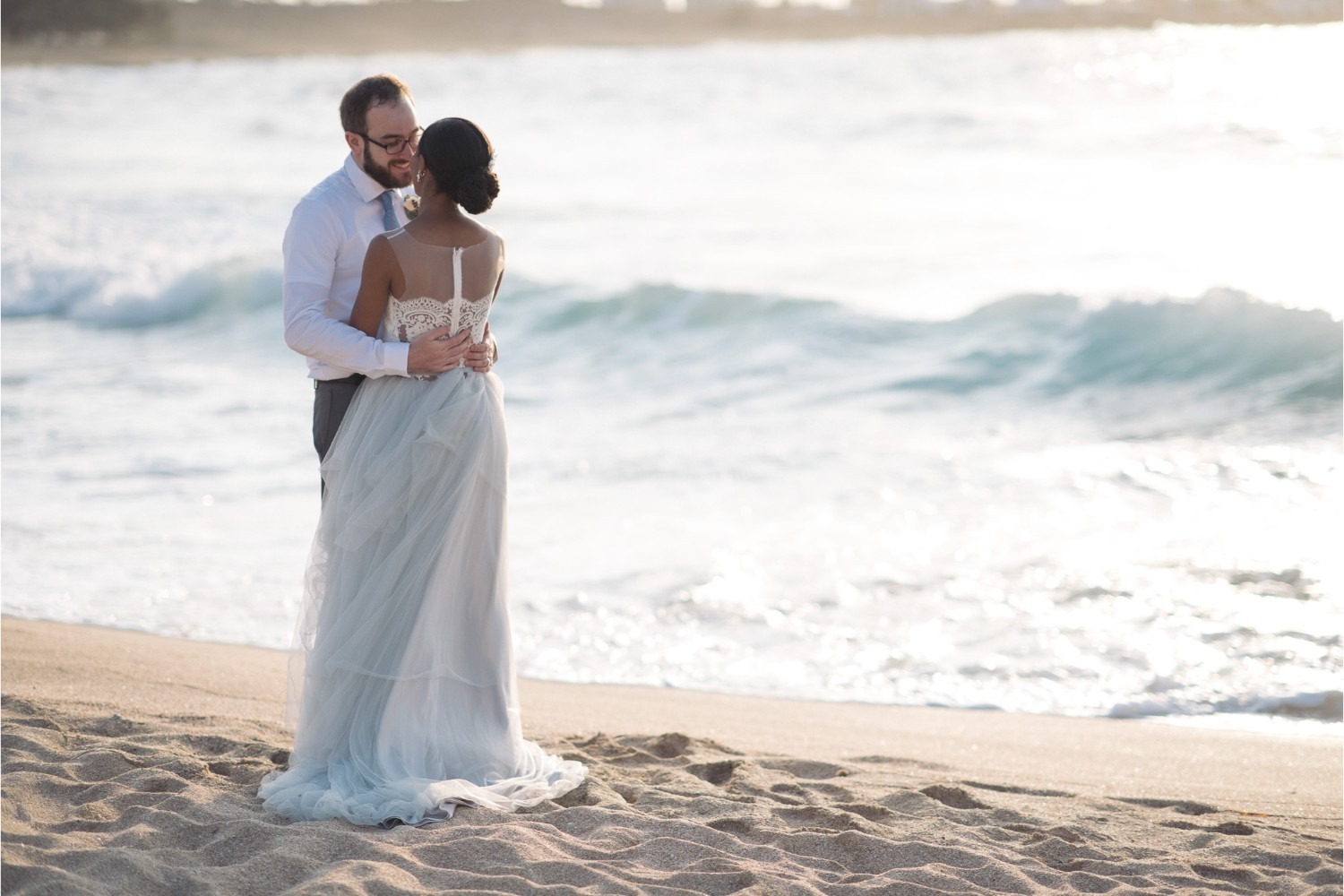 A couple embrace on a Cretan beach as waves roll in behind them, Crete for Love