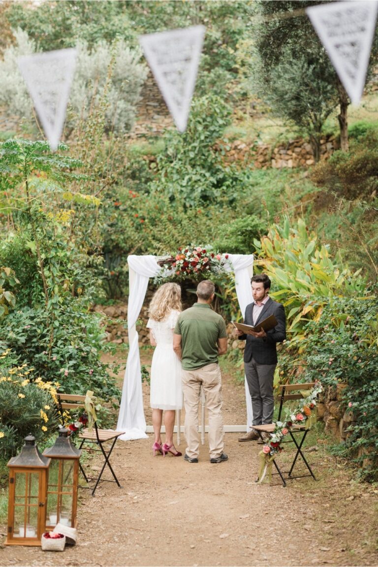 A small ceremony arch with a floral top set among trees and bunting, Crete for Love
