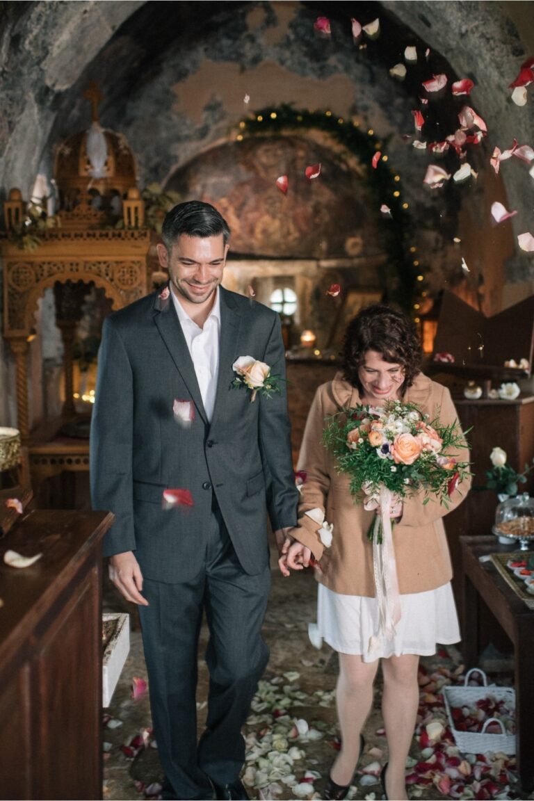 A couple leave a small stone chapel under thrown flower petals, Crete for Love
