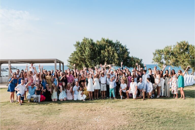 Guests cheer for a group photograph on a seaside lawn, Crete for Love
