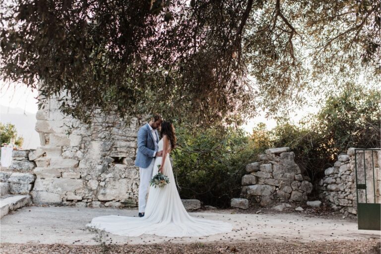 A couple stand under an olive tree beside old stone ruins, Crete for Love