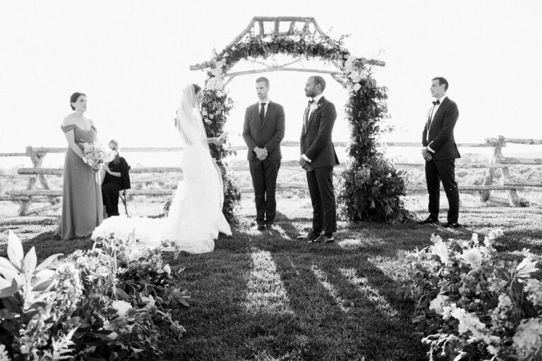 A couple exchanging vows beneath a floral arch among flower beds, Wyoming, Cristina Verger Event Planning and Production