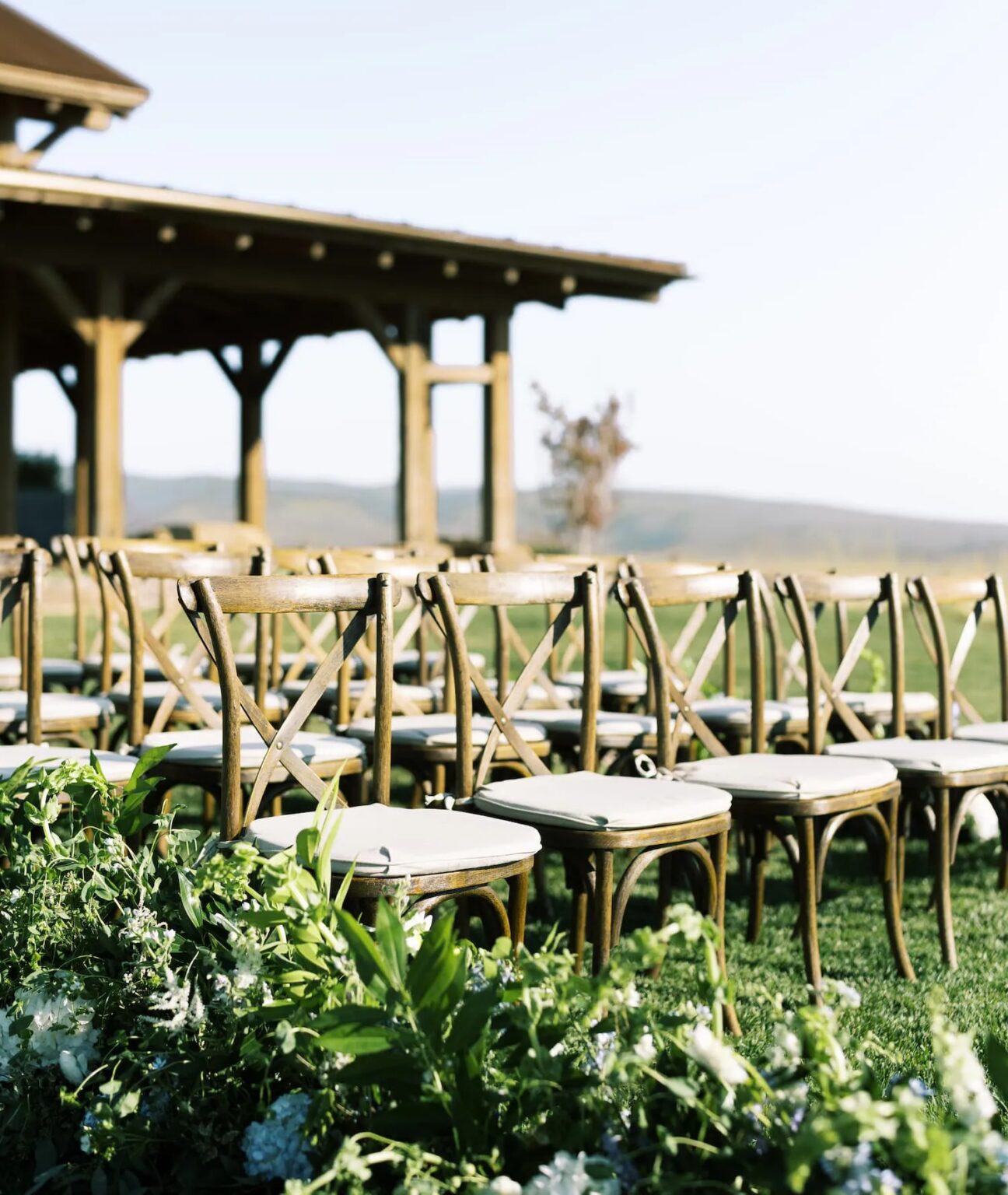Wooden cross-back chairs lined up on the lawn beside a timber pavilion, Wyoming, Cristina Verger Event Planning and Production