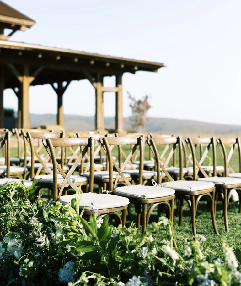 Wooden cross-back chairs lined up on the lawn beside a timber pavilion, Wyoming, Cristina Verger Event Planning and Production