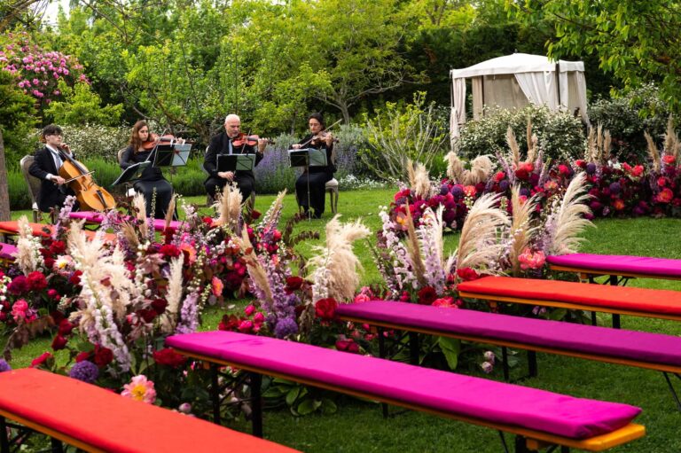 Colourful benches and a quartet in a Tuscan garden ceremony set with pink and red flowers, Cristina Verger Event Planning and Production