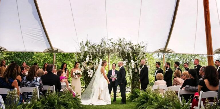A ceremony under a white tent with a greenery-covered arch and guests seated, Connecticut, Cristina Verger Event Planning and Production