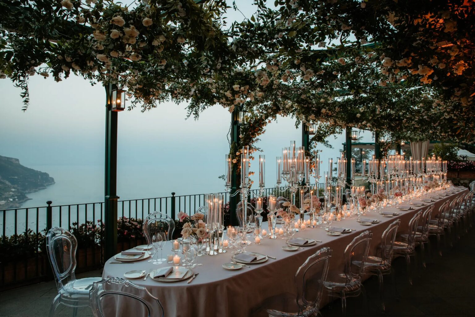 A long table set with candelabras under a flowering pergola on a clifftop terrace above the sea, Ravello