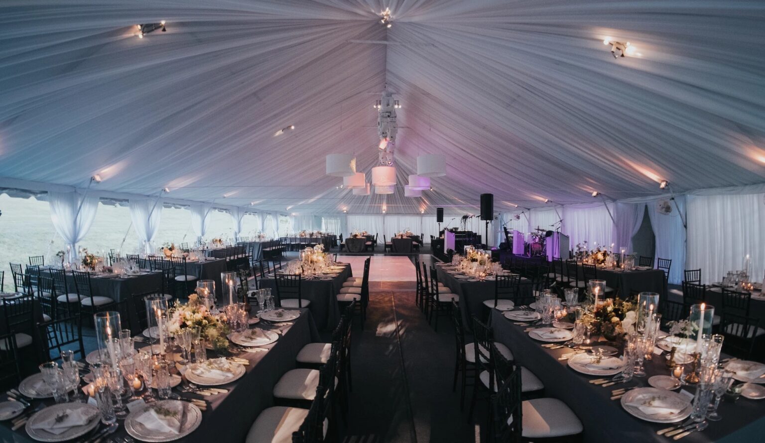 A tented reception with long dark tables, flowers and chandeliers, Vermont