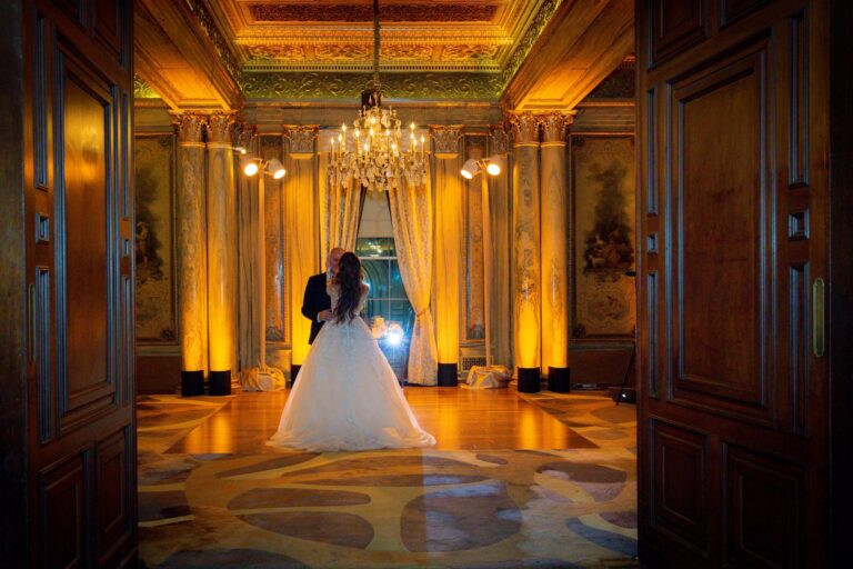 A bride in a gown standing in a gilded hotel doorway with warm uplighting, New York, Cristina Verger Event Planning and Production